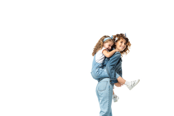 side view of mother piggybacking daughter in denim outfit isolated on white - Valokuva, kuva