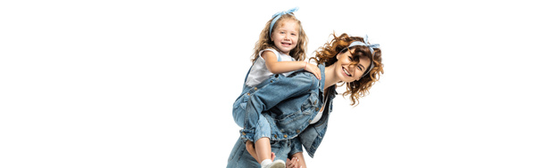 side view of laughing mother piggybacking daughter in denim outfit isolated on white, panoramic shot - Fotó, kép