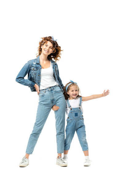 daughter in denim outfit hugging mother leg with outstretched hand isolated on white - Foto, Imagen