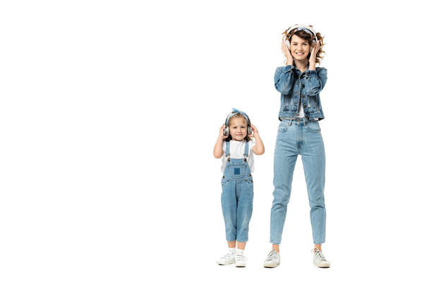 mother and daughter in denim outfits listening music in headphones isolated on white - Φωτογραφία, εικόνα