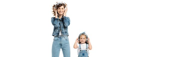 母親と娘は白いパノラマショットで隔離されたヘッドフォンで音楽を聴くデニムの衣装で - 写真・画像