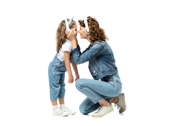 side view of mother and daughter in denim outfits listening music in headphones face to face isolated on white - Φωτογραφία, εικόνα