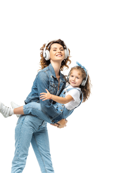 moeder holding dochter en luisteren muziek in hoofdtelefoon geïsoleerd op wit - Foto, afbeelding