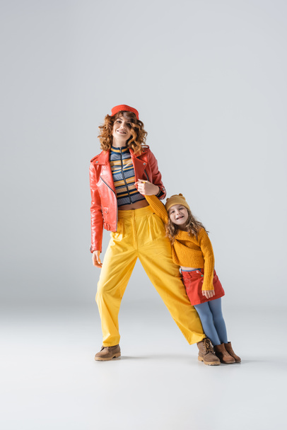 mother and daughter in colorful red and yellow outfits posing on grey background - Φωτογραφία, εικόνα