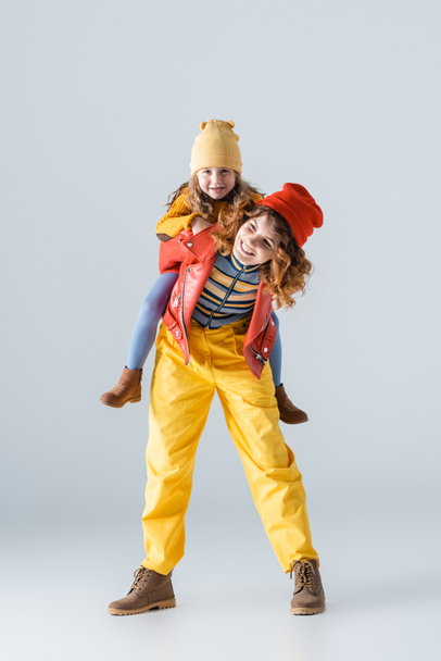 mother and daughter in colorful red and yellow outfits piggybacking on grey background - Zdjęcie, obraz