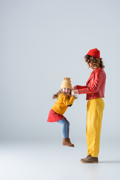 side view of mother and daughter in colorful red and yellow outfits playing on grey background - Foto, Imagen