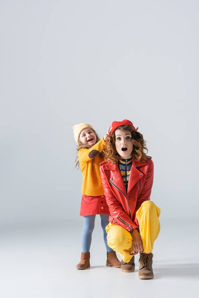 mother and daughter in colorful red and yellow outfits having fun on grey background - Zdjęcie, obraz