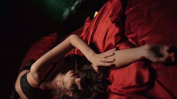 Красива волосся жінка перетинає руки на атласних простирадлах. Сексуальна дівчина лежить на шовковому ліжку
 - Фото, зображення