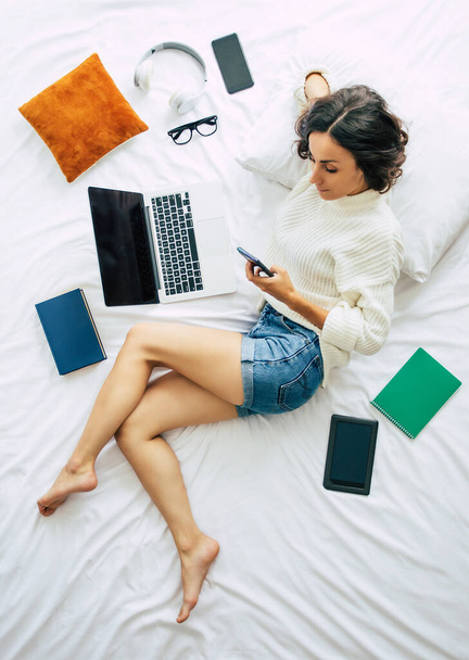 Happy young beautiful woman is working on the laptop while lying on bed at home. Top view or above photo - Foto, Imagem