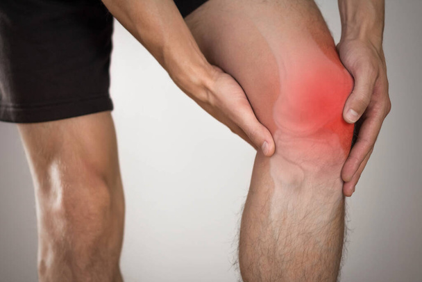Pain in the knee of a man. Highlighted in red. On a gray background. Close up. - Foto, immagini