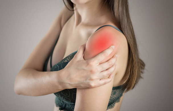 Shoulder pain in a woman. Highlighted in red. On a gray background. Close up. - 写真・画像