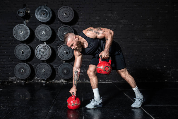 Young strong sweaty fit muscular man with big muscles doing back muscles workout with kettlebells in the gym as hardcore cross training - 写真・画像