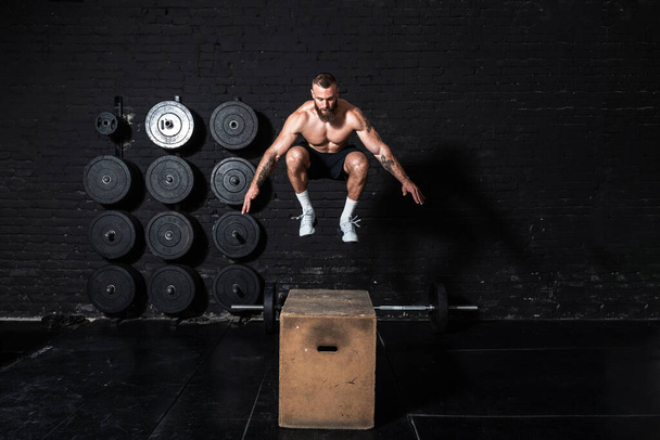 Mladý silný fit zpocený svalnatý muž s velkými svaly dělat box skok cvičení v tělocvičně jako hardcore kříž školení - Fotografie, Obrázek