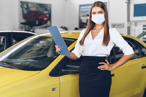Woman car seller standing near new car wearing protective face mask - Фото, изображение