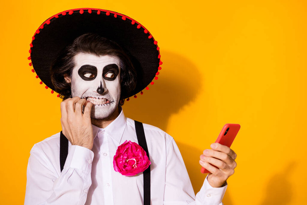 Close-up portrait of his he nice painted creepy worried nervous guy caballero using gadget browsing fake news blogging post biting nails isolated bright vivid shine vibrant yellow color background - Foto, Imagen