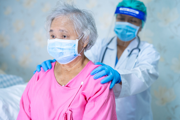 Врач, проверяющий пациента пожилой или пожилой азиатки в маске для защиты от инфекции и убивающий вирус Коронавируса Ковид-19. - Фото, изображение