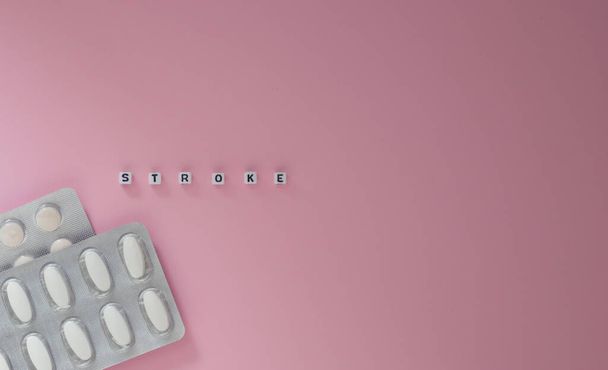 Concept van gezondheid, cardiologie, hartziekte. Woorden STROKEN op witte blokjes, tabletten in blisterverpakkingen op een roze achtergrond. Vlakke lay, kopieerruimte. - Foto, afbeelding