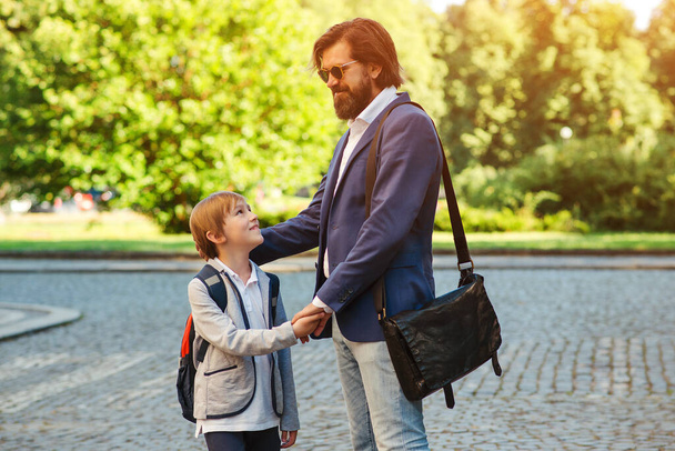 School boy with backpack holding his daddy hand while going to school. Back to school. Father takes his son to school. Parenthood, relationship, childhood. - Zdjęcie, obraz