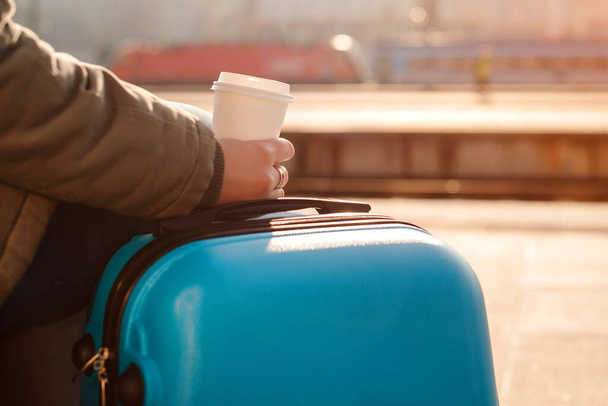Tren bekleyen turist kadın. Bavullu kadın. Tren istasyonunda elinde bir fincan kahve tutan bir kadın. Trenle seyahat et. Yaşam tarzı, seyahat, tatil. - Fotoğraf, Görsel