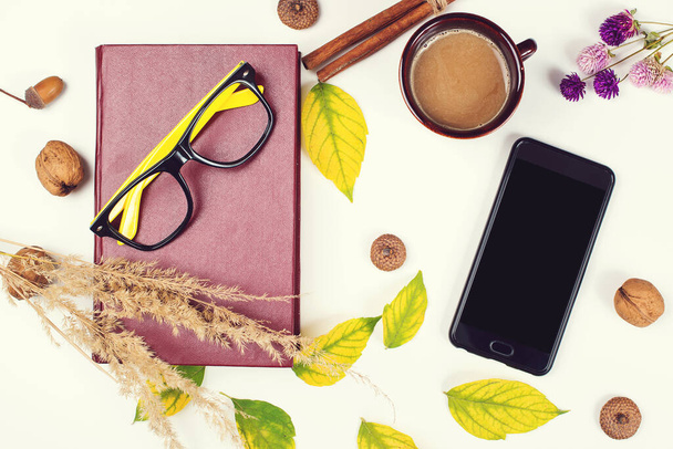 Autumn background with cup of coffee, book, mobile phone and autumn leaves. Mockup with smartphone and autumn decoration. Autumn time for reading. - Photo, Image
