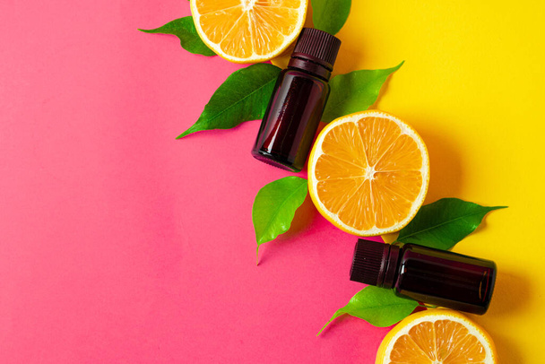 Citrus essential oil. Sliced citrus fruit and aroma bottles on pink background - Photo, image