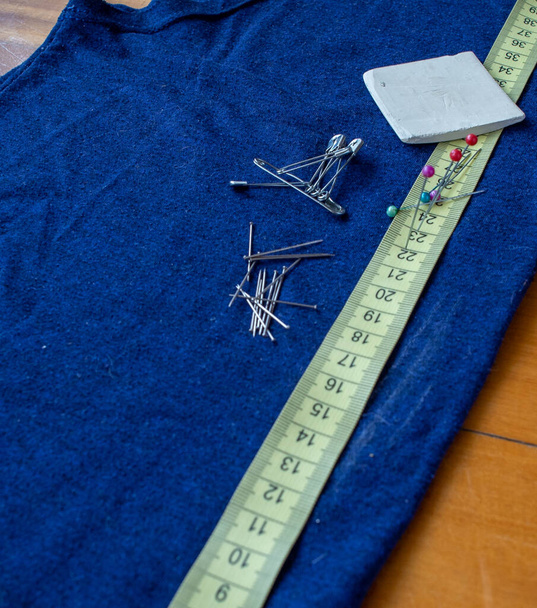 Centimetro sobre una tela azul, con algunos alfileres y una tiza de sastre. - Foto, Imagem