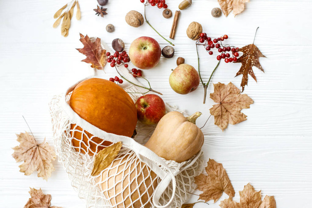 Zero marnotrawstwa Dziękczynienia. Torba na zakupy wielokrotnego użytku z dyniami, jabłkami, jagodami, orzechami i jesiennymi liśćmi na białym drewnianym tle. Ekologiczne jesienne wakacje, jesienne zbiory - Zdjęcie, obraz