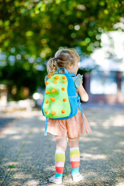 Leuke kleine schattige peuter meisje op haar eerste dag naar de speelschool. Gezonde mooie baby wandelen naar kleuterschool en kleuterschool. Gelukkig kind met rugzak in de stad straat, buiten. - Foto, afbeelding