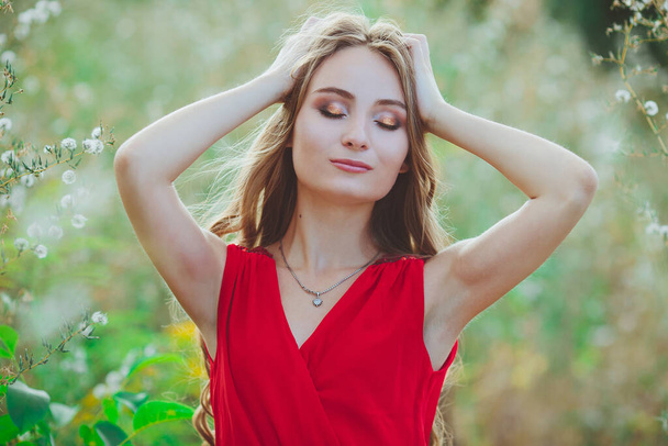 Portrait of a young beautiful girl in a red dress on the summer field outdoors - Foto, imagen
