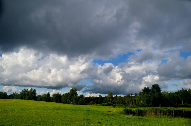 Czarne chmury burzowe latem, Krajobraz z drzewami i łąkami na pierwszym planie na Łotwie. Niskie chmury - Zdjęcie, obraz