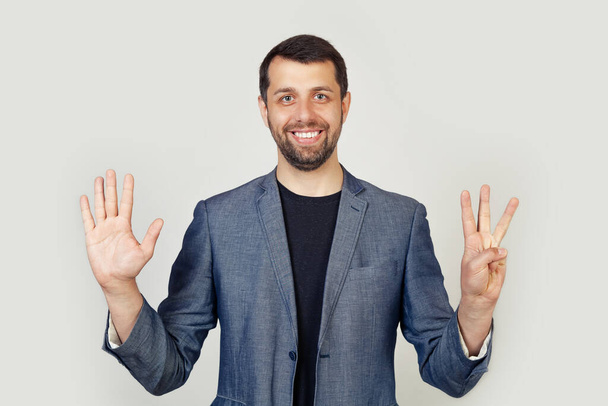 Young businessman man with beard smiling, showing number eight with fingers on hand, smiling confidently and happily, looking into the camera. The man shows eight fingers. Number 8. - Фото, изображение