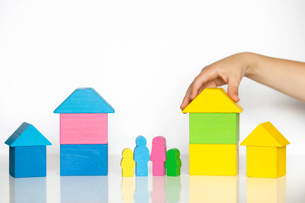 Childs hand building a bright wooden town from multicolored blocks. Wooden figures of people, adults and children. Close up. Learning and development concept. - Photo, Image