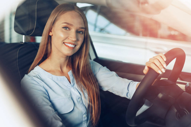 Attractive young woman sitting in new car in showroom - Photo, Image