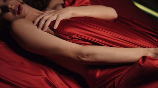 Sexy mains de femme jouant feuille de soie rouge au lit. Fille nue se détendre dans la chambre. - Photo, image