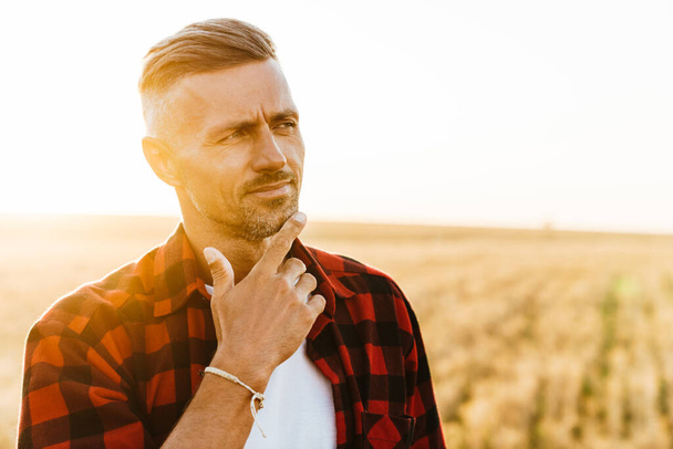Image of thinking focused adult man looking aside while standing at cereal field - Foto, Imagen