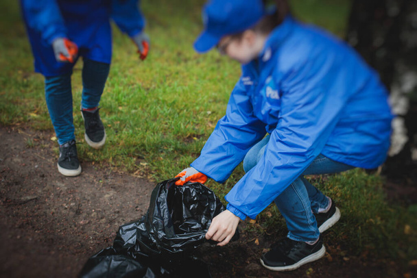 Team group of young people, girls and boys volunteering and participate in community work cleaning day, activists collecting waste, rubbish, garbage and litter in bags in the city park - Фото, изображение