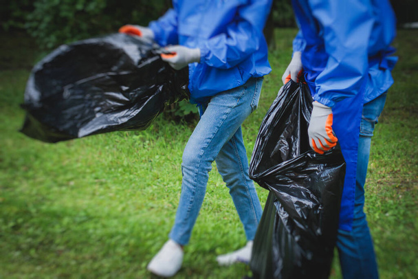 Team group of young people, girls and boys volunteering and participate in community work cleaning day, activists collecting waste, rubbish, garbage and litter in bags in the city park - Fotó, kép