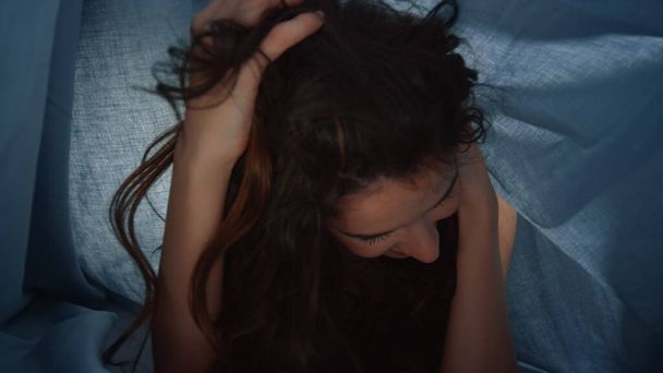 Chica alegre tocando el pelo debajo de la cama cubierta. Mujer feliz posando fondo textil - Foto, Imagen
