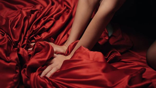 ベッドの上で赤いサテンシートを持っている女性の手。未知の少女は喜びを持っている. - 写真・画像