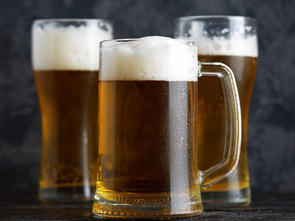 Кружка с пивом и пивные стаканы на темном фоне крупным планом - Фото, изображение