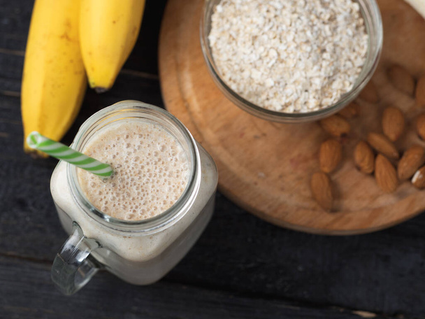 Fresh banana smoothie on a wooden table in a jar . With oatmeal and almonds - Photo, Image
