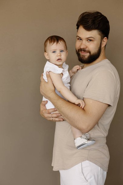 Happy young man holding a smiling 9-10 months old baby, isolated on beige background - Photo, Image