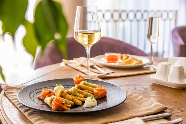 a glass of white wine with a snack. for a snack pancakes with red fish and curd cheese. - Fotoğraf, Görsel