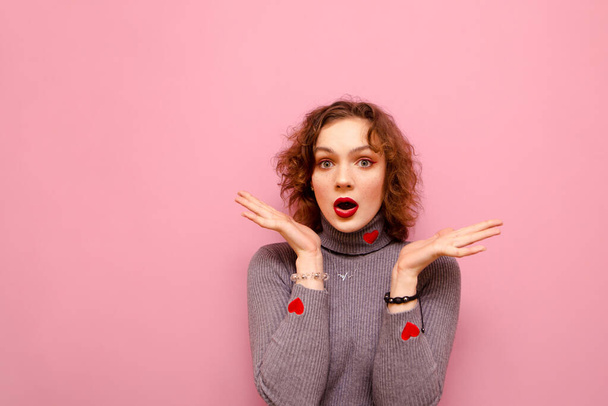 Portrait of bewildered curly girl with surprised face stands on pink background and looks into camera with arms raised. Confused pretty lady isolated on pink. - Foto, immagini