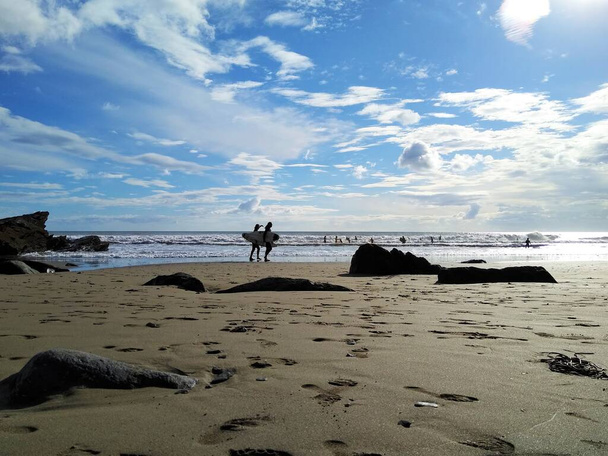 Силуэты людей на пляже, включая двух идущих серферов - Фото, изображение
