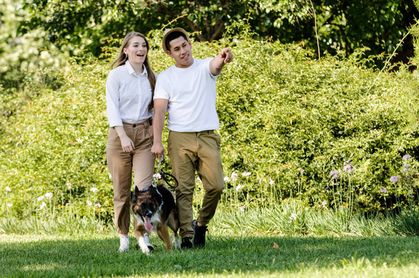 Modernes junges Paar spaziert und spielt mit seinem Hund Border Collie in einem Park - Foto, Bild