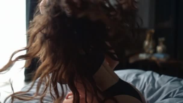 Gyönyörű nő, aki megérinti a haját a hálószobában. Bájos lány ül térden az ágyon. - Felvétel, videó