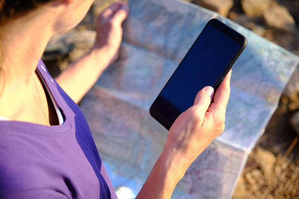 Vrouw op zoek naar een kaart en telefoon - Foto, afbeelding