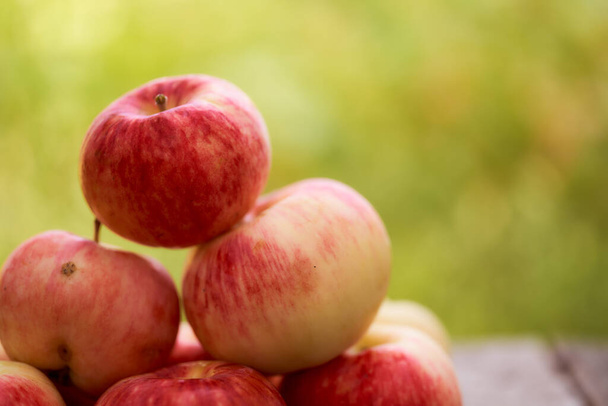 Red apples lie on a wooden board. Green blurred background. Close-up. High quality photo - Photo, Image