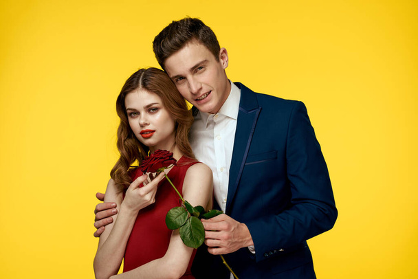 milenci muž a žena s červenou růží v rukou objímání na žlutém pozadí romantika vztah láska rodina - Fotografie, Obrázek
